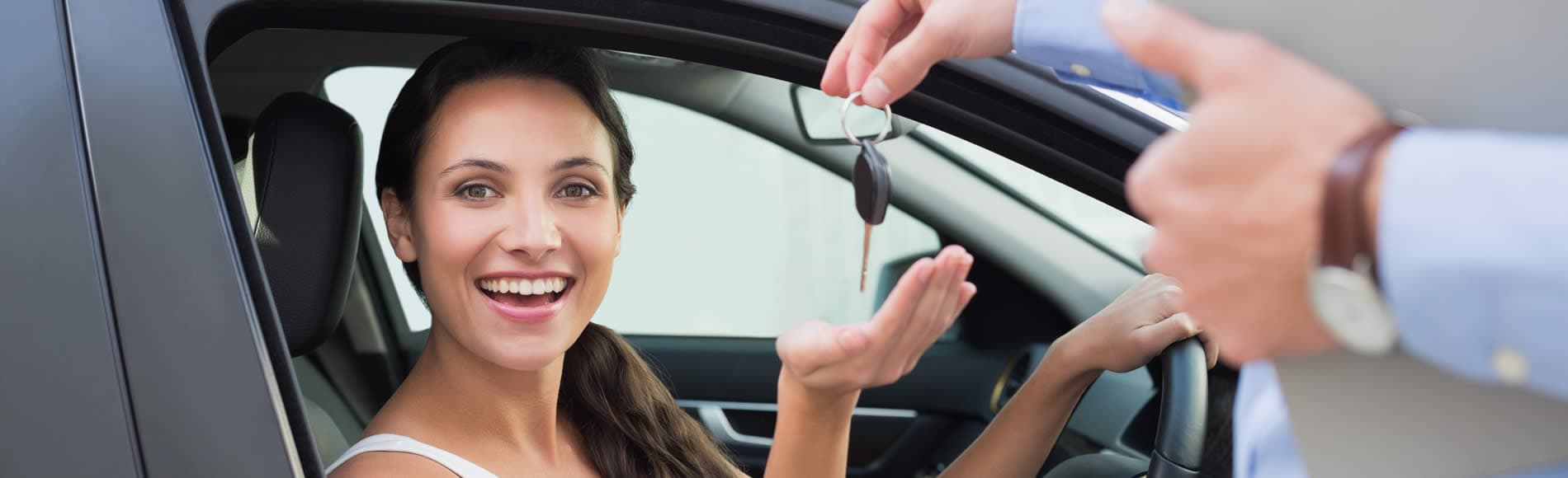 Man handing over the key to a new car to a young woman sitting in the driver's seat